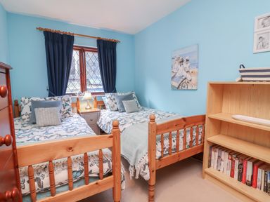 A bedroom with two single wooden beds a small lamp on a nightstand and a wooden bookshelf at Old Farm Cottage in Woolacombe