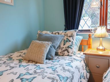 A bedroom with a bed featuring butterfly patterned bedding and pillows beside a nightstand with a lamp at Old Farm Cottage in Woolacombe