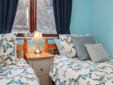 A bedroom with twin beds butterflies on bedding a nightstand and a lamp at Old Farm Cottage in Woolacombe