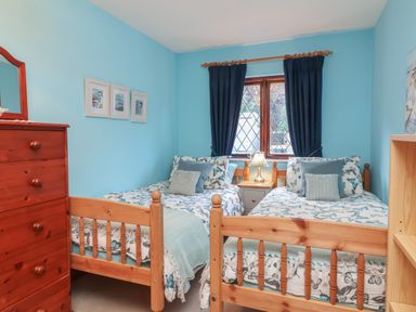 A bedroom with two single wooden beds a wooden dresser and a window with dark curtains at Old Farm Cottage in Woolacombe