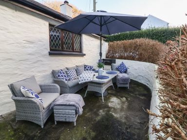 An outdoor seating area with wicker furniture cushions a table umbrella and plants at Old Farm Cottage in Woolacombe