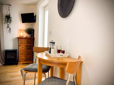 A small wooden dining table with two chairs and a tray with drinks next to a wooden cabinet and a wall-mounted TV at The Studio in Crackington Haven