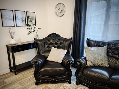A living room with black leather armchairs and a black console table with vases near a window with dark curtains at Trelawne Near Crackington Haven