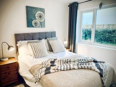 A bedroom with a bed pillows bedside tables lamps and a window with curtains at Trelawne Near Crackington Haven
