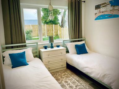 A bedroom with two single beds a dresser and a window with curtains at Trelawne Near Crackington Haven