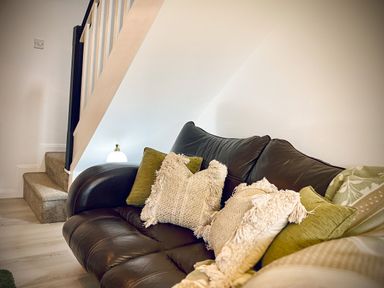 A living room with a dark leather sofa with cushions under a staircase at Penkenna in Crackington Haven
