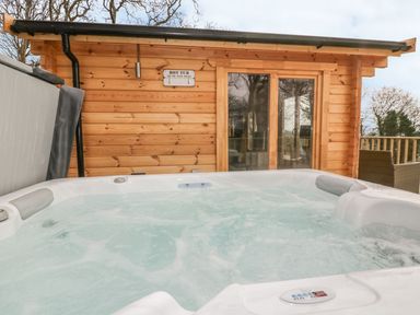 An outdoor hot tub with bubbling water next to a wooden cabin with glass doors at Little Orchard Lodge in Goonhavern