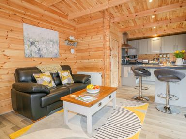 A living area with a black leather sofa and coffee table and a kitchen with two bar stools at Little Orchard Lodge in Goonhavern
