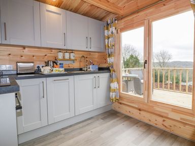 A kitchen with cabinets countertop sink and sliding glass door opening to a balcony with chairs at Little Orchard Lodge in Goonhavern