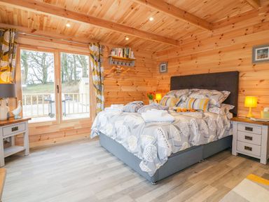 A bedroom with a double bed side tables and a sliding glass door at Little Orchard Lodge in Goonhavern