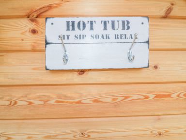 A wooden wall with a white sign that reads hot tub sit sip soak relax with two metal hooks attached
