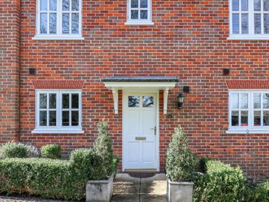 A brick house facade with a white front door and four white framed windows with shrubs in front at Bay Tree Cottage Peasenhall