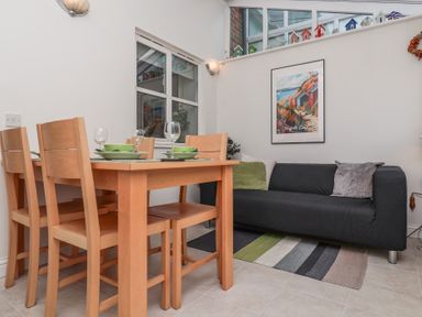 A dining area with wooden table and chairs next to a black sofa with pillows and a striped rug at Bay Tree Cottage in Peasenhall