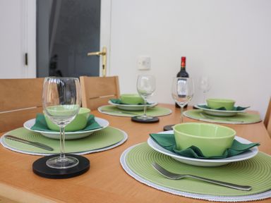 A dining table set with green bowls plates napkins and placemats with wine glasses and a wine bottle at Bay Tree Cottage in Peasenhall