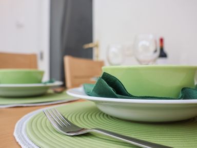 A dining table set with green bowls white plates green napkins and a fork at Bay Tree Cottage in Peasenhall