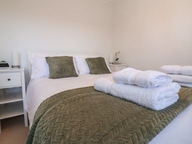 A bedroom with a bed with pillows and folded towels on a green blanket at Bay Tree Cottage in Peasenhall