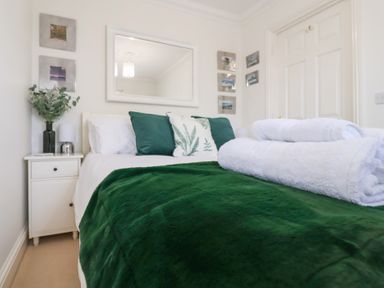 A bedroom with a bed covered with a green blanket and white towels on top at Bay Tree Cottage in Peasenhall