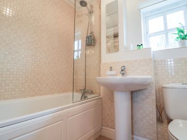 A bathroom with a bathtub shower combination a white pedestal sink a toilet and a window with a plant on the sill at Bay Tree Cottage in Peasenhall