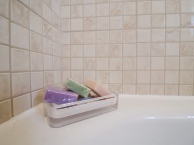 A soap dish with three wrapped soap bars on the edge of a bathtub with tiled walls