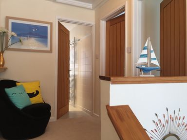A hallway with three wooden doors a black chair with colorful pillows a framed picture on the wall and a model sailboat on a wooden railing at Maceley Kingsbridge
