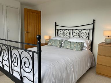 A bedroom with a black metal bed frame white bedding two floral pillows wooden door wooden drawers with lamps on each side of the bed at Maceley in Kingsbridge