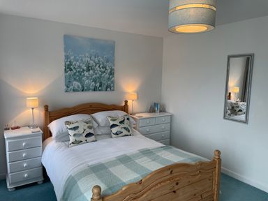 A bedroom with a wooden bed frame white bedding and two bedside tables with lamps at Maceley in Kingsbridge