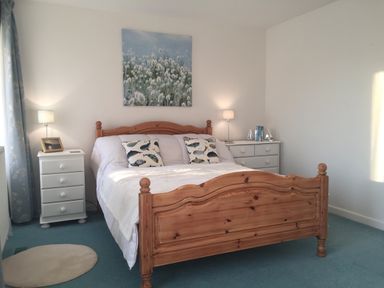 A bedroom with a wooden bed white bedding two fish patterned pillows two white nightstands each with a lamp and decor items and floral curtains at Maceley Kingsbridge