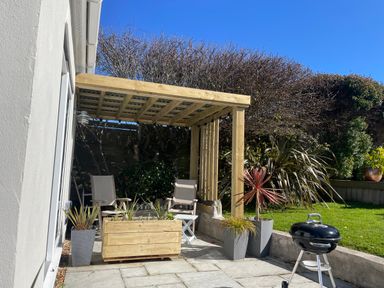 A patio area with wooden pergola chairs planter boxes and a barbecue grill at Maceley in Kingsbridge