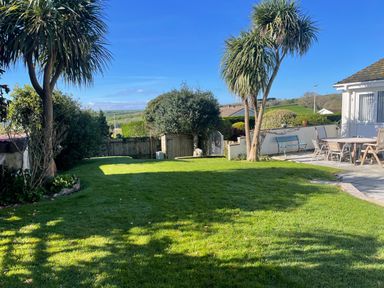 A garden with a grass lawn trees a dining table with chairs and a bench near a house at Maceley in Kingsbridge