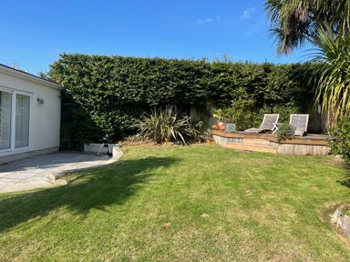 A backyard garden with grass lawn wooden deck with two lounge chairs plants and a small barbecue near a white building at Maceley in Kingsbridge