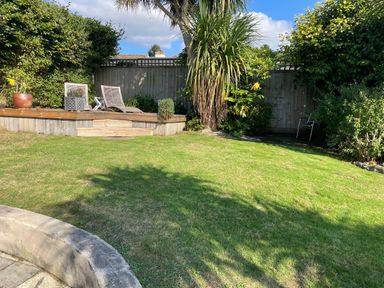 A garden with a wooden deck with two lounge chairs plants and a palm tree at Maceley in Kingsbridge