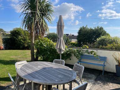 An outdoor garden area with a round wooden table and metal chairs next to a closed patio umbrella and a blue bench at Maceley in Kingsbridge
