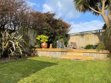 A garden with a wooden deck, potted plants, two chairs, and a small table at Maceley in Kingsbridge