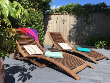 Two wooden lounge chairs with striped cushions and towels on a deck with plants and a wooden fence at Maceley in Kingsbridge