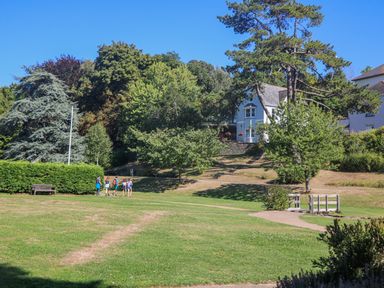 A park with a group of people walking on grass near trees and houses in the background at Maceley in Kingsbridge