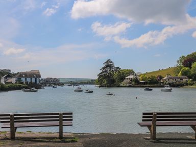 A view of a river with boats and houses on the shore with benches in the foreground at Maceley in Kingsbridge