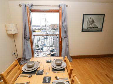 A dining area with a wooden table set for four near a window overlooking boats at 15 Sovereign House in Milford Haven