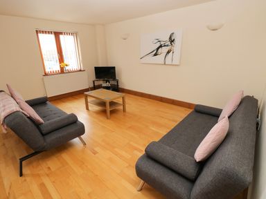 A living room with two gray sofas a wooden coffee table a small TV and a window with flowers at 15 Sovereign House in Milford Haven