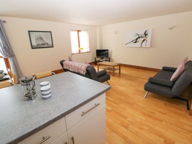 A living room with two sofas a coffee table and a TV viewed from a kitchen counter at 15 Sovereign House in Milford Haven