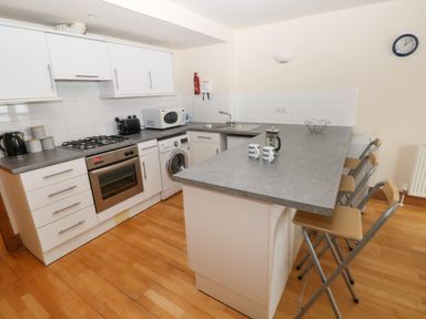 A kitchen with white cabinets wooden floor a countertop with three stools and kitchen appliances at 15 Sovereign House in Milford Haven