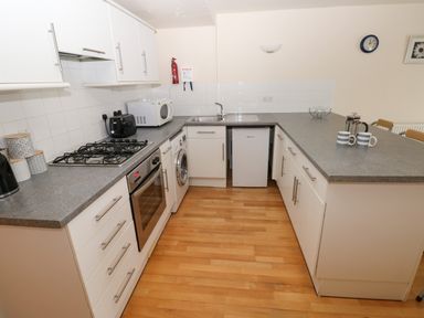 A kitchen with white cabinets a gas stove an oven a washing machine a microwave a toaster and a countertop at 15 Sovereign House in Milford Haven