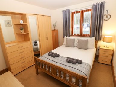 A bedroom with a double bed wooden furniture and a window with gray curtains at 15 Sovereign House in Milford Haven