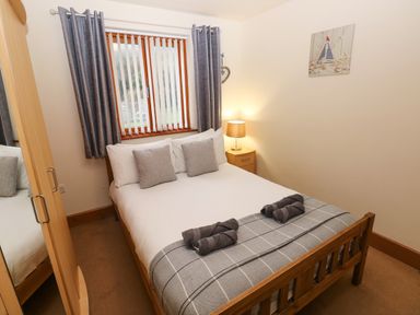 A bedroom with a double bed two rolled towels bedside table with lamp window with blinds and curtains wardrobe 15 Sovereign House Milford Haven
