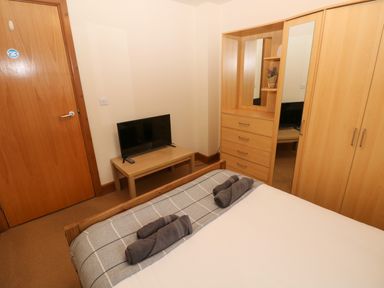 A bedroom with a bed towels a television on a table and a wooden wardrobe at 15 Sovereign House in Milford Haven