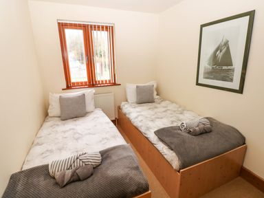 A bedroom with two single beds with pillows and folded towels under a window with blinds at 15 Sovereign House in Milford Haven