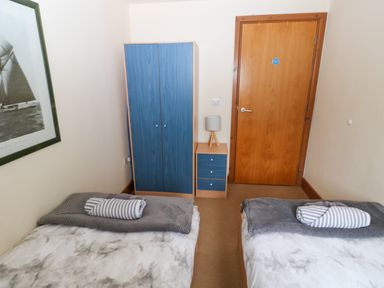 A bedroom with two single beds a blue wardrobe a small blue bedside table with a lamp and a wooden door at 15 Sovereign House in Milford Haven