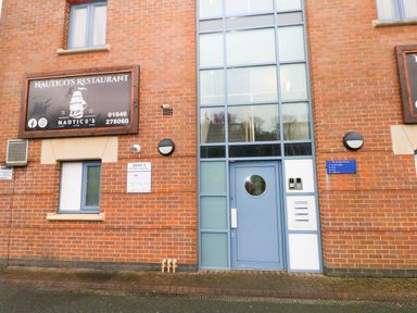 The entrance to a building with a blue door and a sign for Nautico's Restaurant on a brick wall at 15 Sovereign House in Milford Haven
