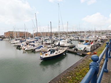 A marina with multiple moored sailboats and yachts near brick buildings and a blue railing at 15 Sovereign House in Milford Haven