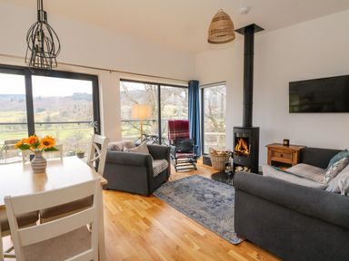 A living room with sofas a wood stove and large windows showing a landscape at Dundarach in Aberfeldy