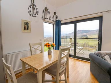 A dining area with a wooden table and four chairs next to large glass sliding doors showing a balcony and a mountain view at Dundarach in Aberfeldy